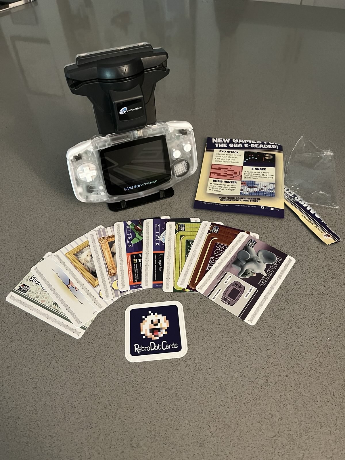 Colorful game cards fanned out in front of a Game Boy Advance with e-Reader cartridge and the opened plastic packaging for the cards.