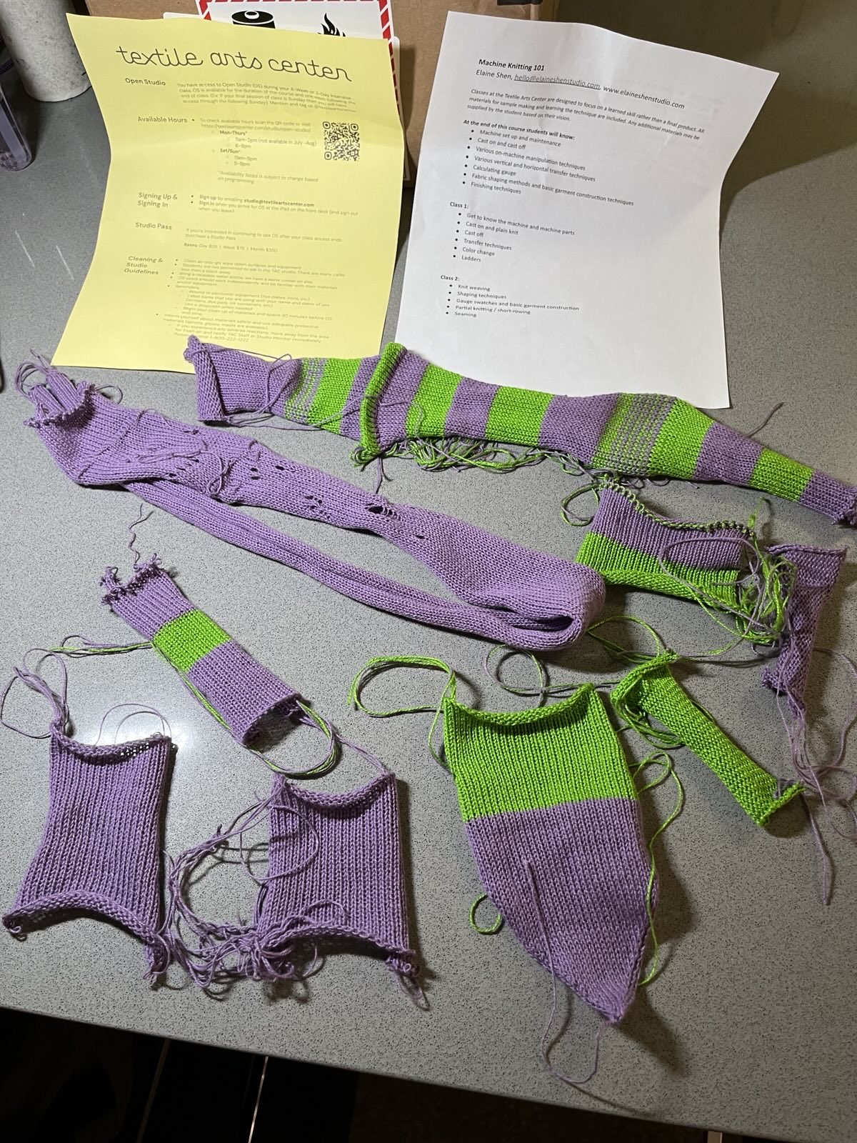 A gray countertop covered in messy machine knit samples of purple and green yarn