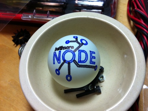 Baltimore Node logo rendered on a ping-pong ball in blue and black. It rests in a small dish with some nuts and bolts.