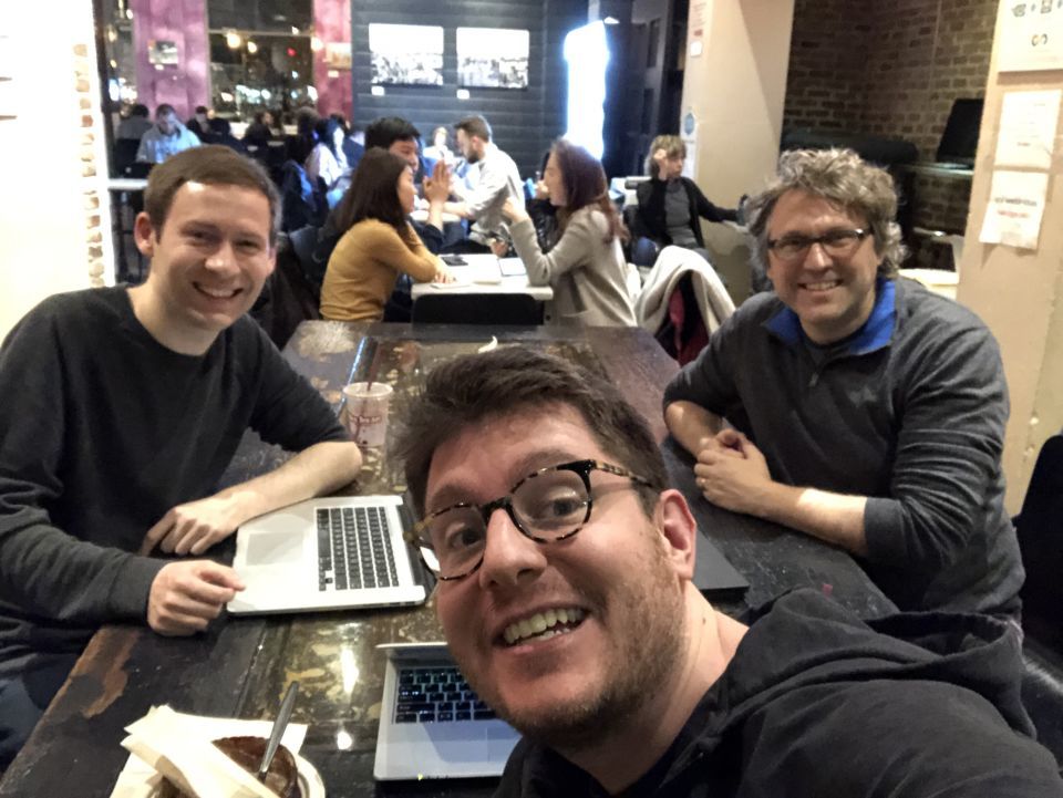 Dmitri, Marty, and Matt smile for the camera in front of a background of a busy coffee shop.