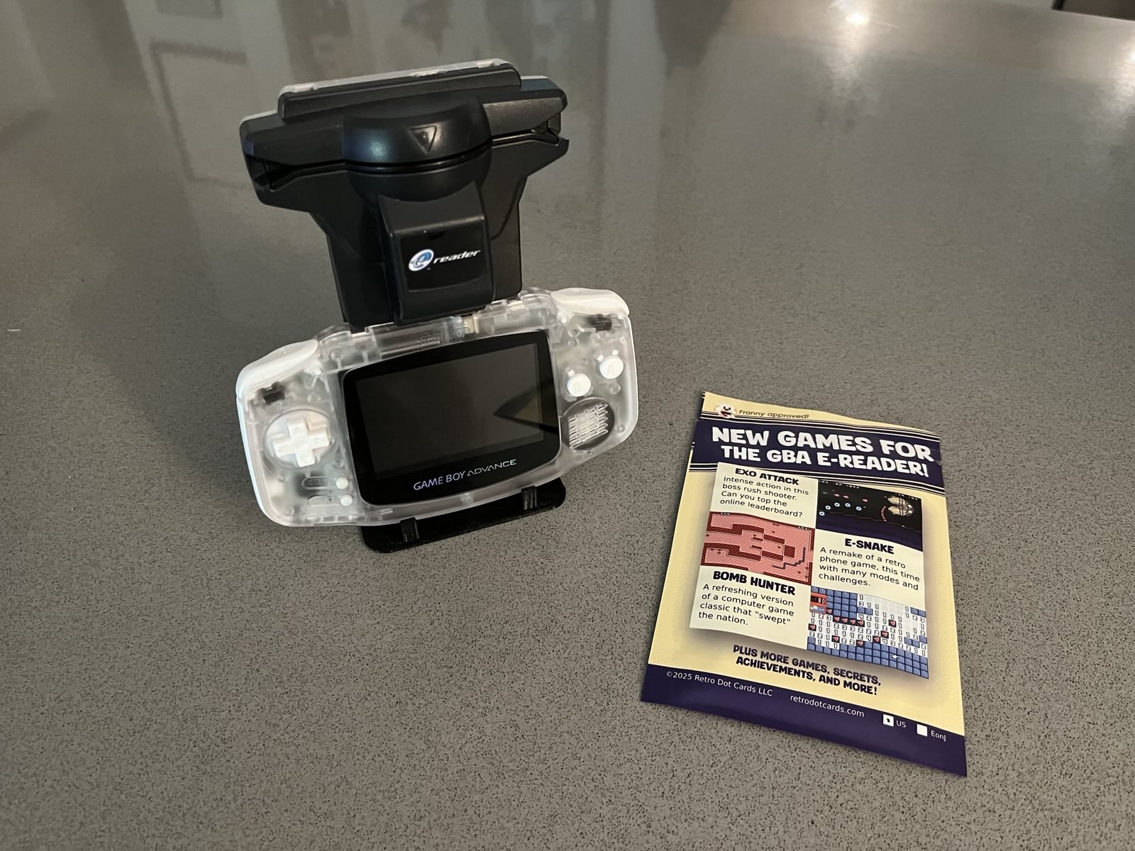 A Nintendo Game Boy Advance with e-Reader cartridge next to a sealed pack. The pack reads 'New games for the GBA e-reader'.